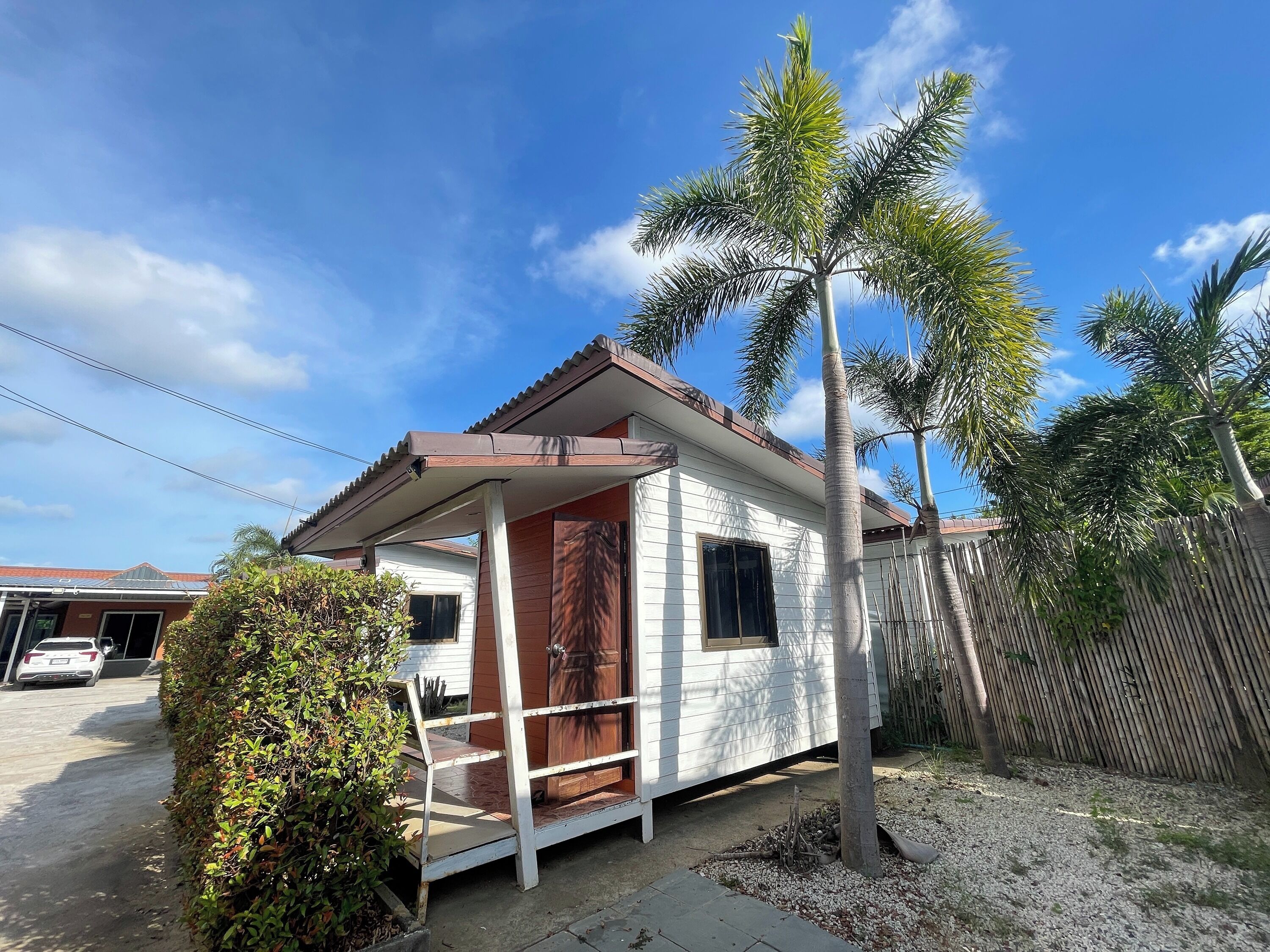 A small house with a porch, a wooden fence, and a palm tree.