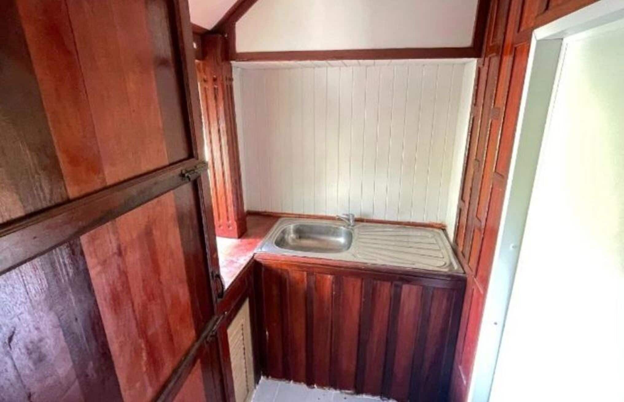 A small, narrow bathroom with wooden walls and a single sink.