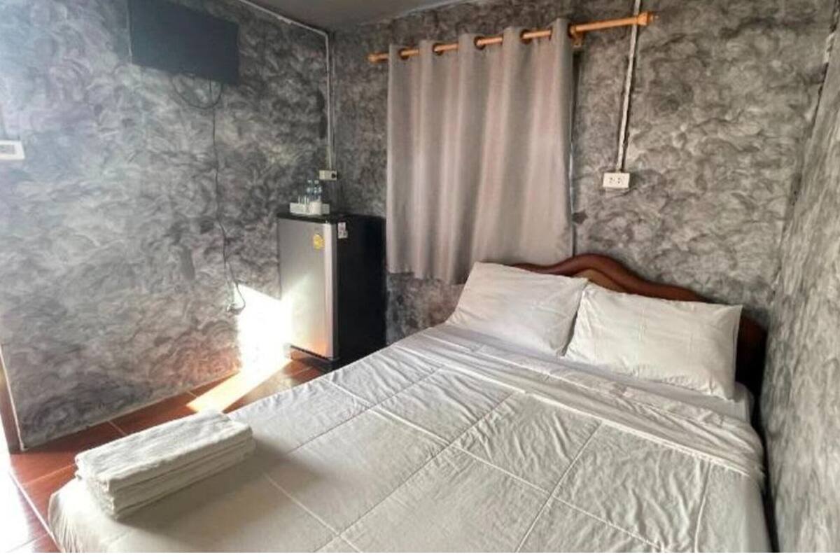 A bedroom with a bed, a small bedside table, a wall-mounted heater, and a window with curtains.