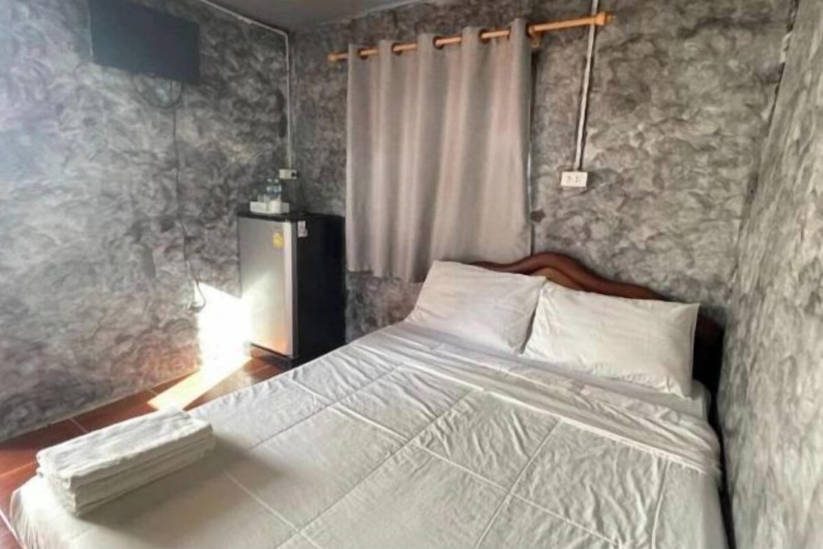A room with a bed, a wooden headboard, a small cabinet, and a curtain.