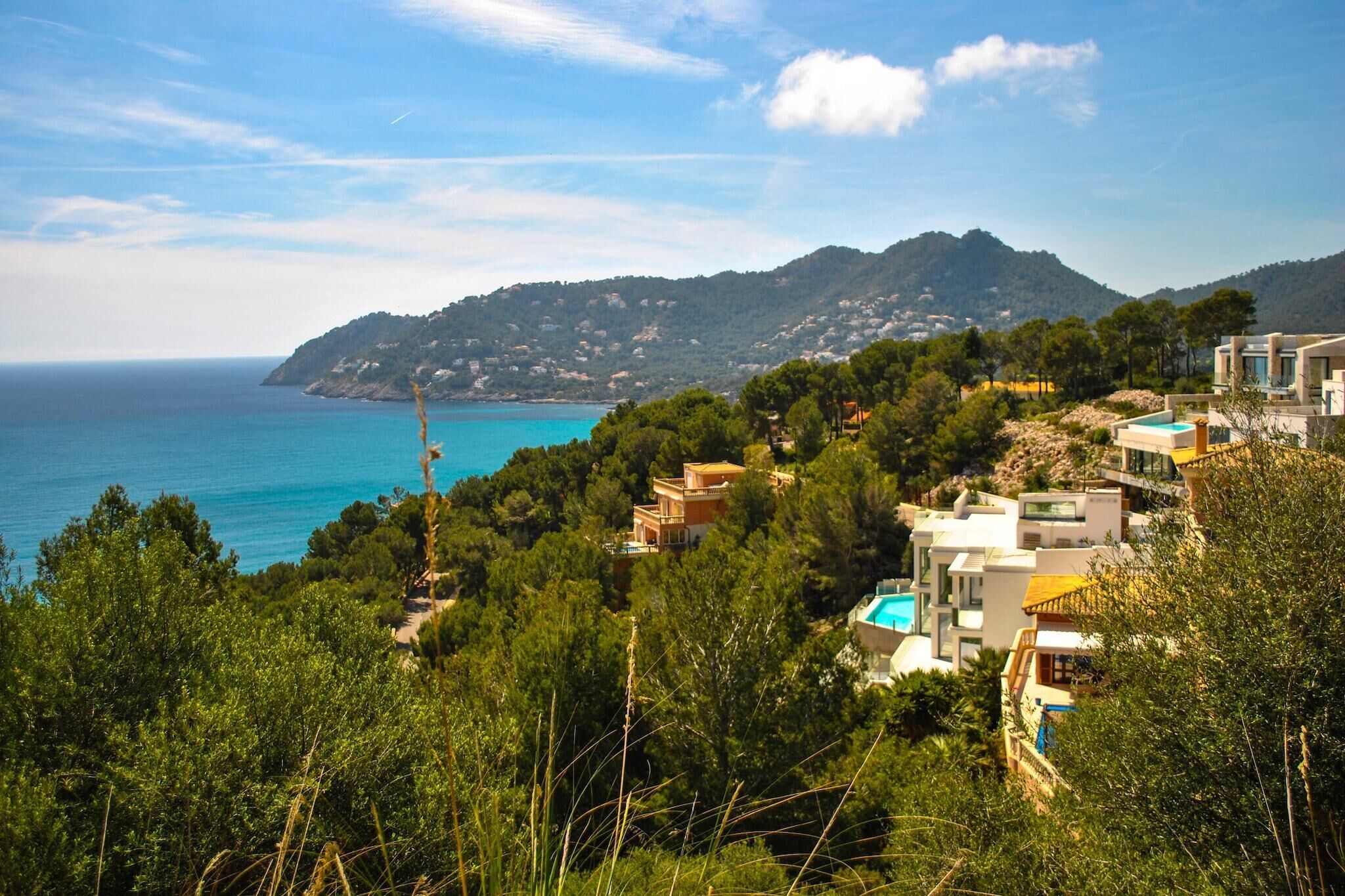 A coastal property with a pool, modern architecture, and a view of the sea and hills.