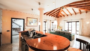 A spacious kitchen with a wooden island, a dining area with a green sofa, and a staircase leading to an upper level. - Villa in Canyamel with Bay Views and Pool (Canyamel)