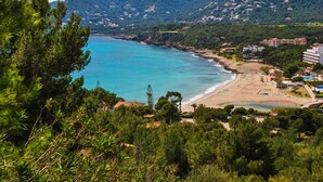Küstenlandschaft mit Strand, Gebäuden und Bergen im Hintergrund.