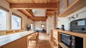 Une cuisine moderne avec des poutres en bois, un coin repas avec une longue table et des chaises, et un four à micro-ondes posé sur le plan de travail.