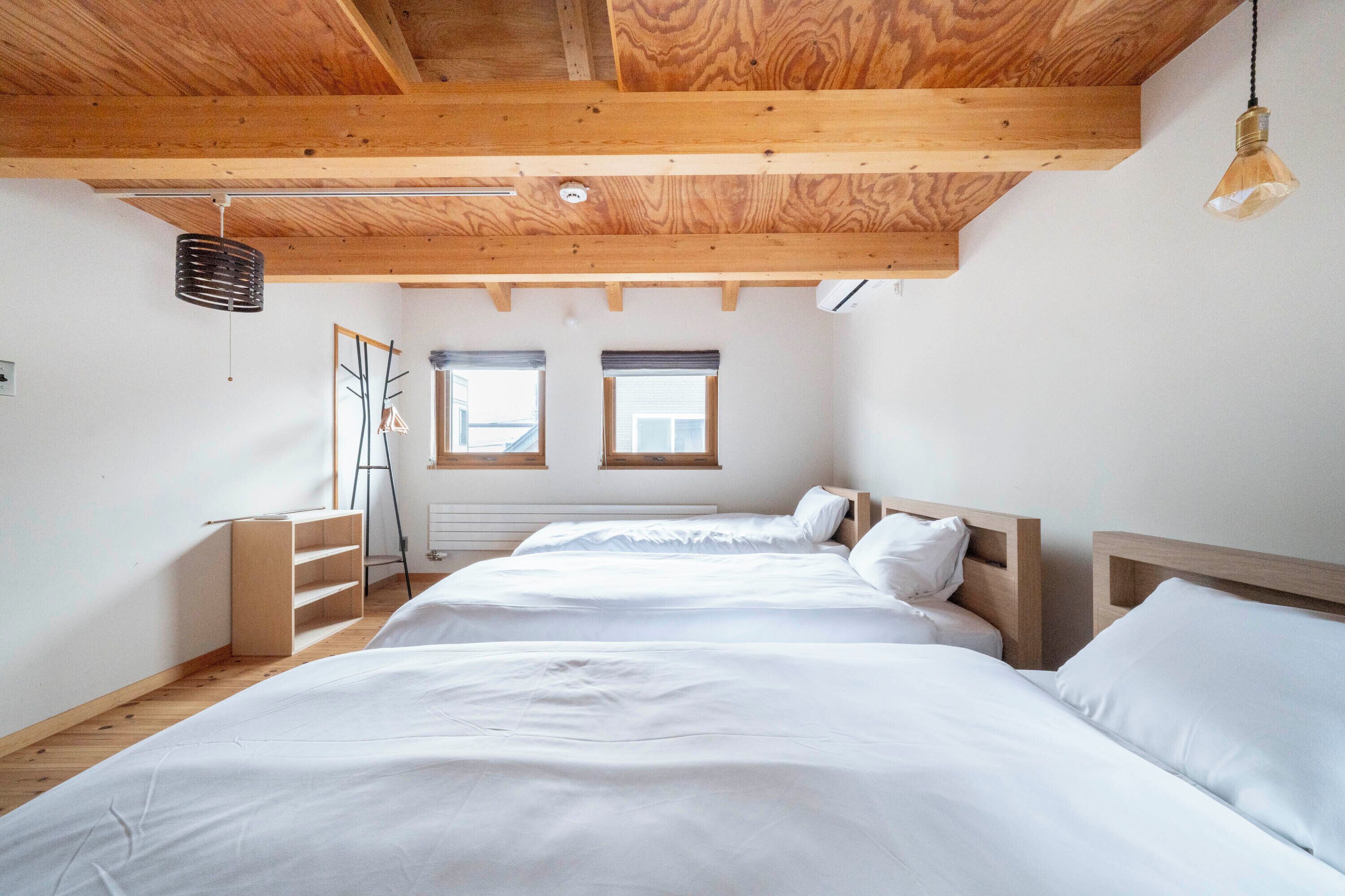 A bedroom with two beds, wooden beams, a ladder, and two windows.