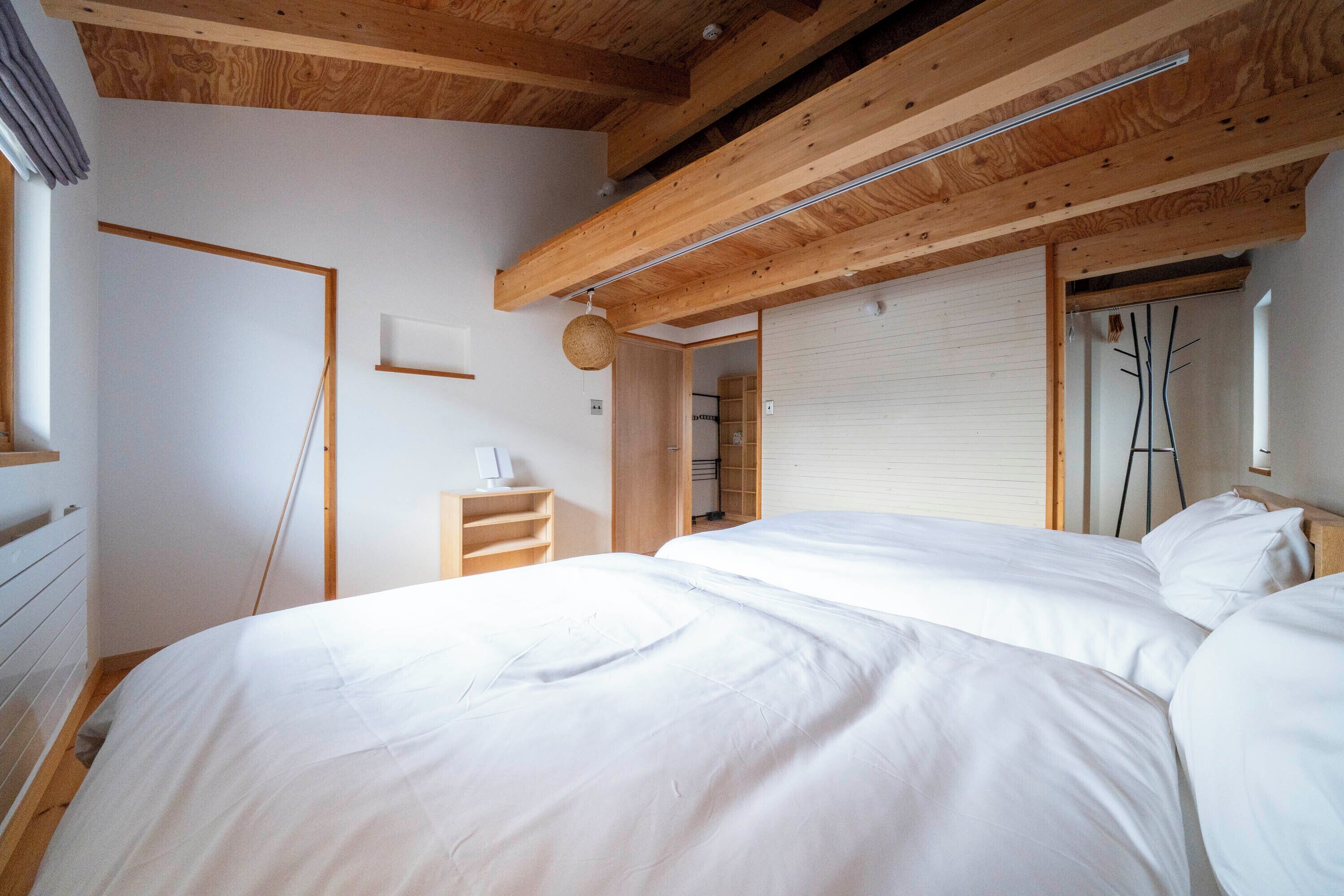 Un dormitorio con una cama grande, vigas de madera en el techo y una pared blanca.