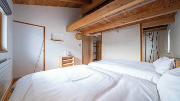 Un dormitorio con una cama grande, vigas de madera en el techo y una pared blanca.
