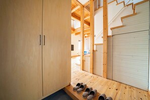 Un interior de madera con un zapatero, una escalera y una puerta cerrada.