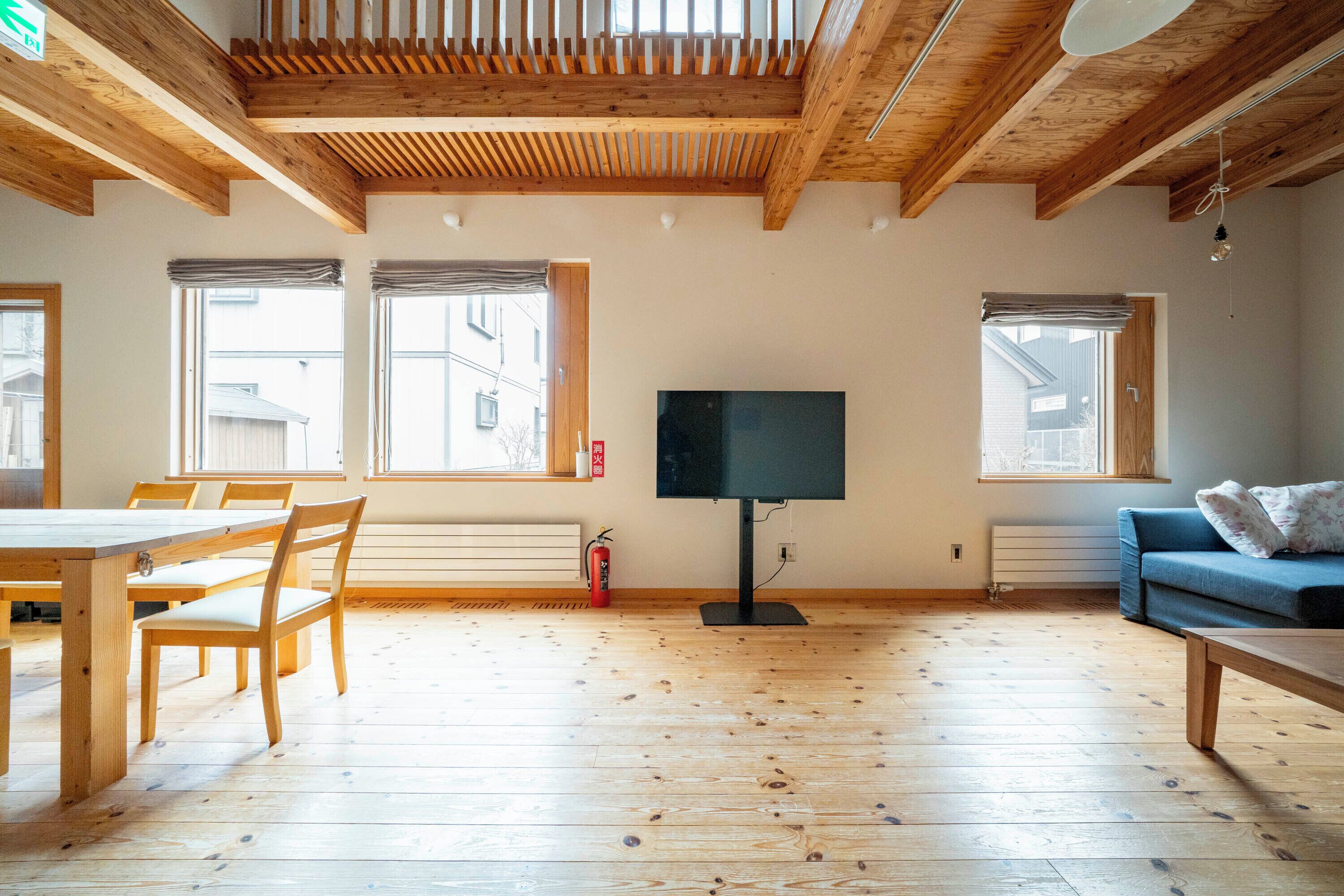 Una habitación amplia con pisos de madera, una mesa grande, sillas, un sofá azul y un televisor de pantalla plana.
