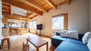 Un vaste espace de vie doté d ’un plancher en bois, d’un canapé bleu agrémenté de coussins à motifs floraux, d’une table basse en bois et d’une cuisine en arrière-plan.