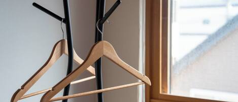 Un perchero de madera con dos perchas al lado de una pared cerca de una ventana.
