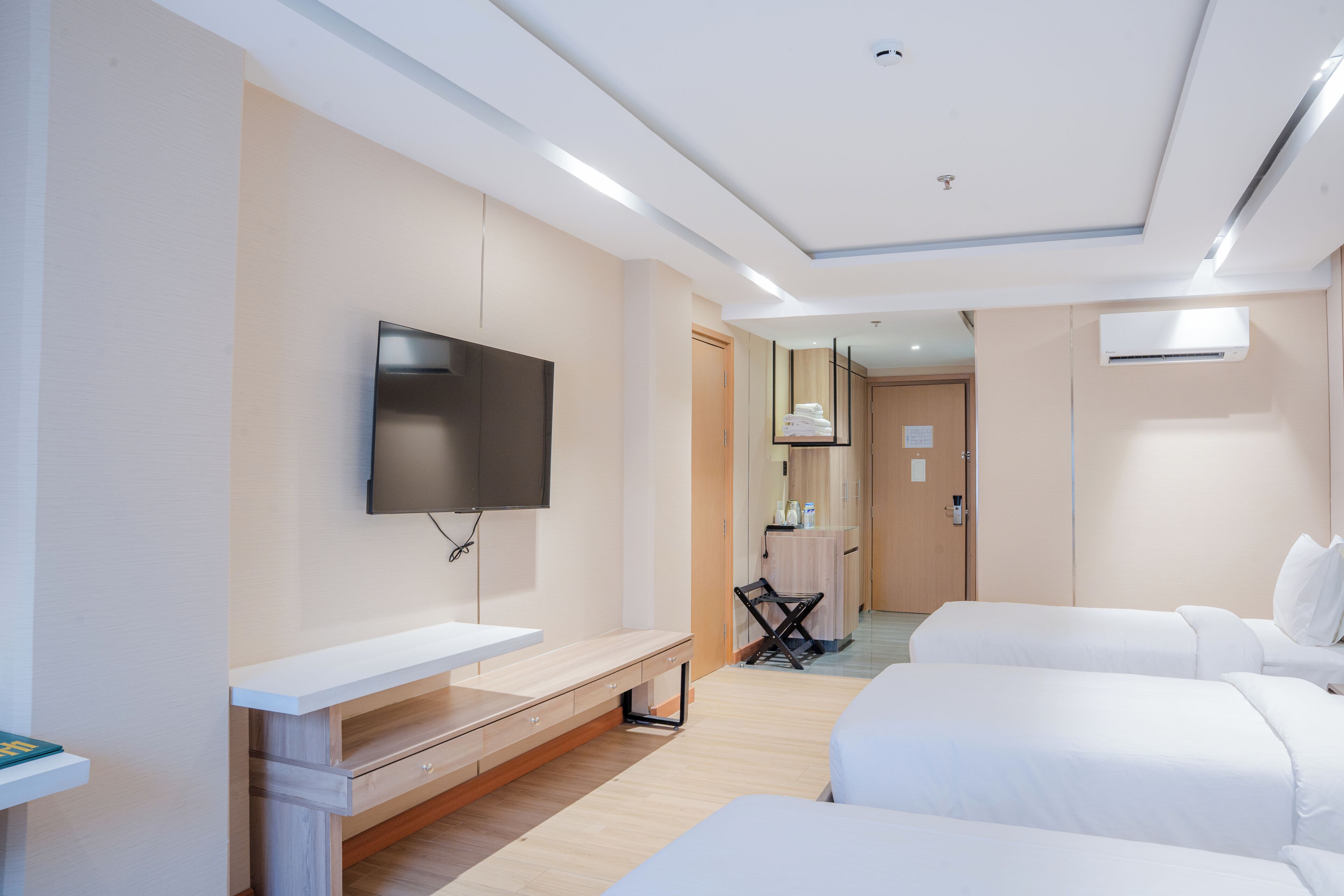 A modern hotel room with a flat-screen TV, a desk, two beds, a mirror, and an air conditioning unit.