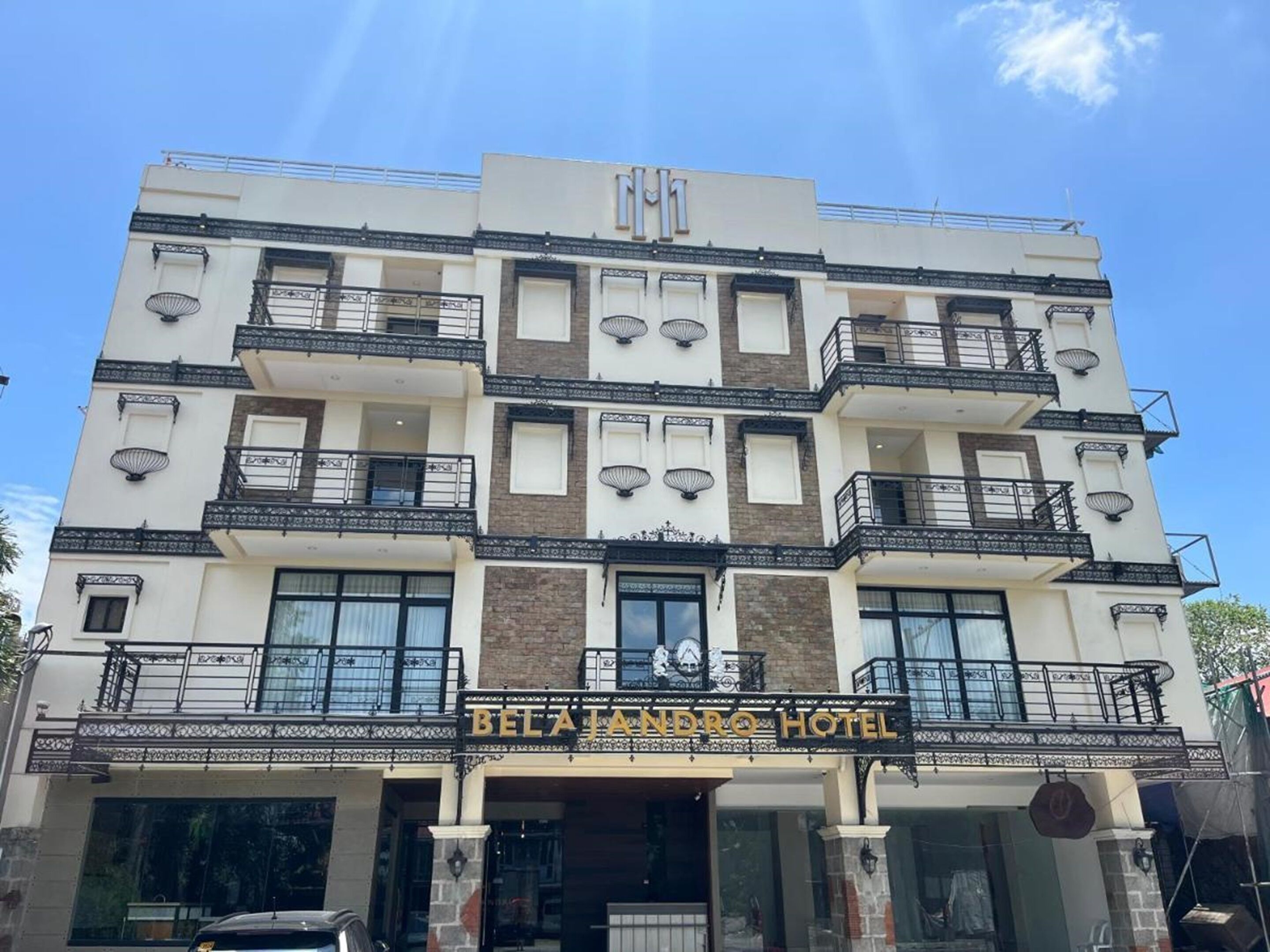 Un hôtel à plusieurs étages doté de balcons, une enseigne indiquant « HÔTEL BELAJANDRO » et un ciel dégagé.