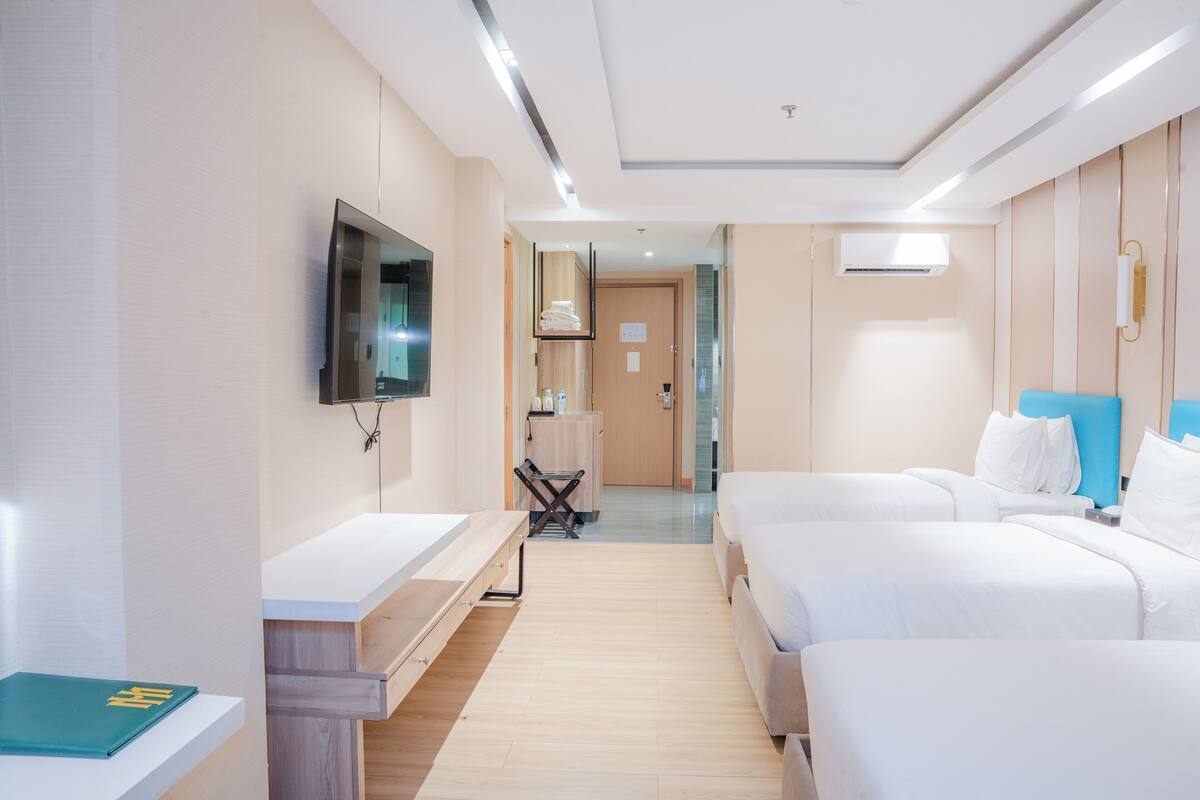 A hotel room with a TV, a desk, two beds, and a bathroom in the background.