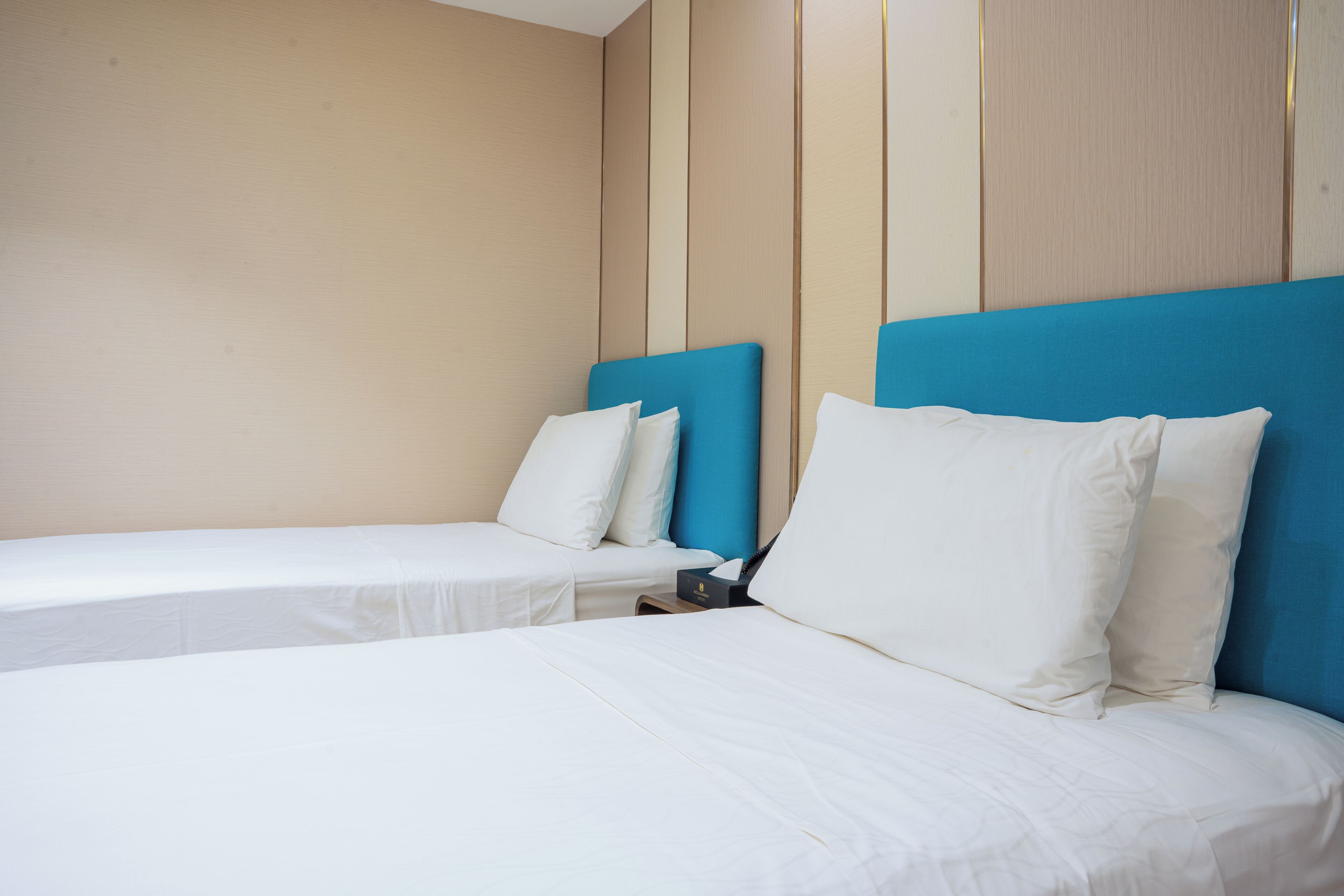 Dos camas individuales con ropa blanca y cabeceros azules en una habitación de hotel.