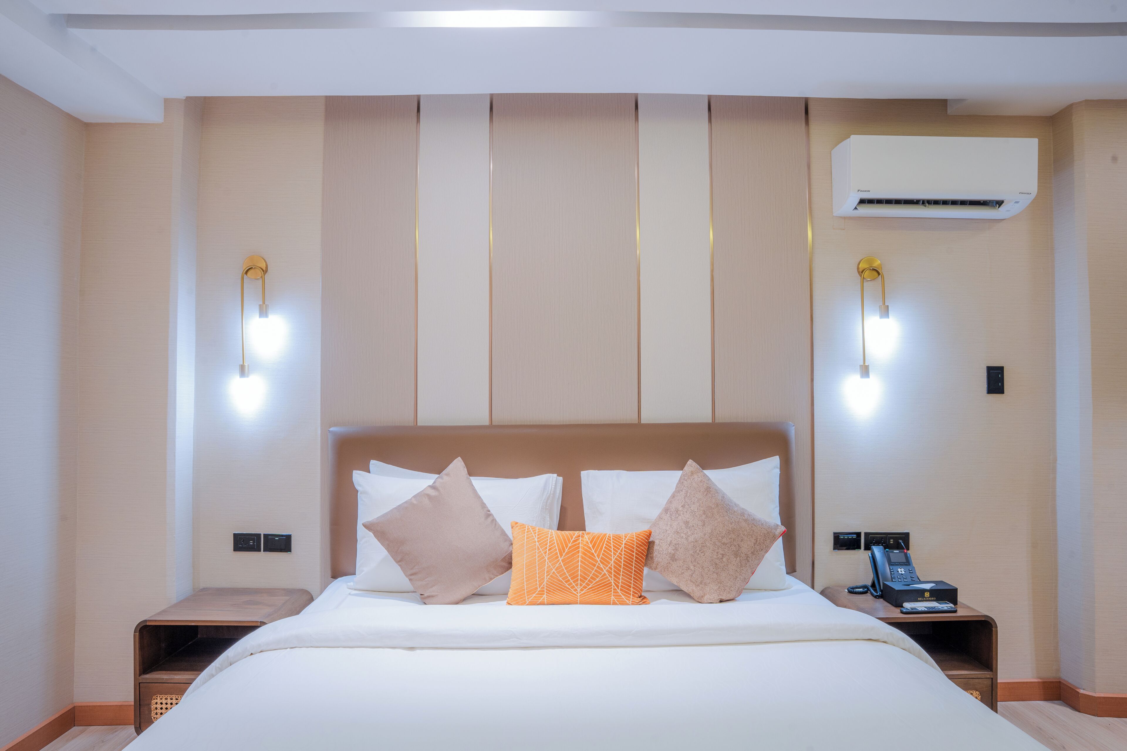A hotel room with a large bed, two bedside tables, an air conditioning unit, and wall-mounted lights.