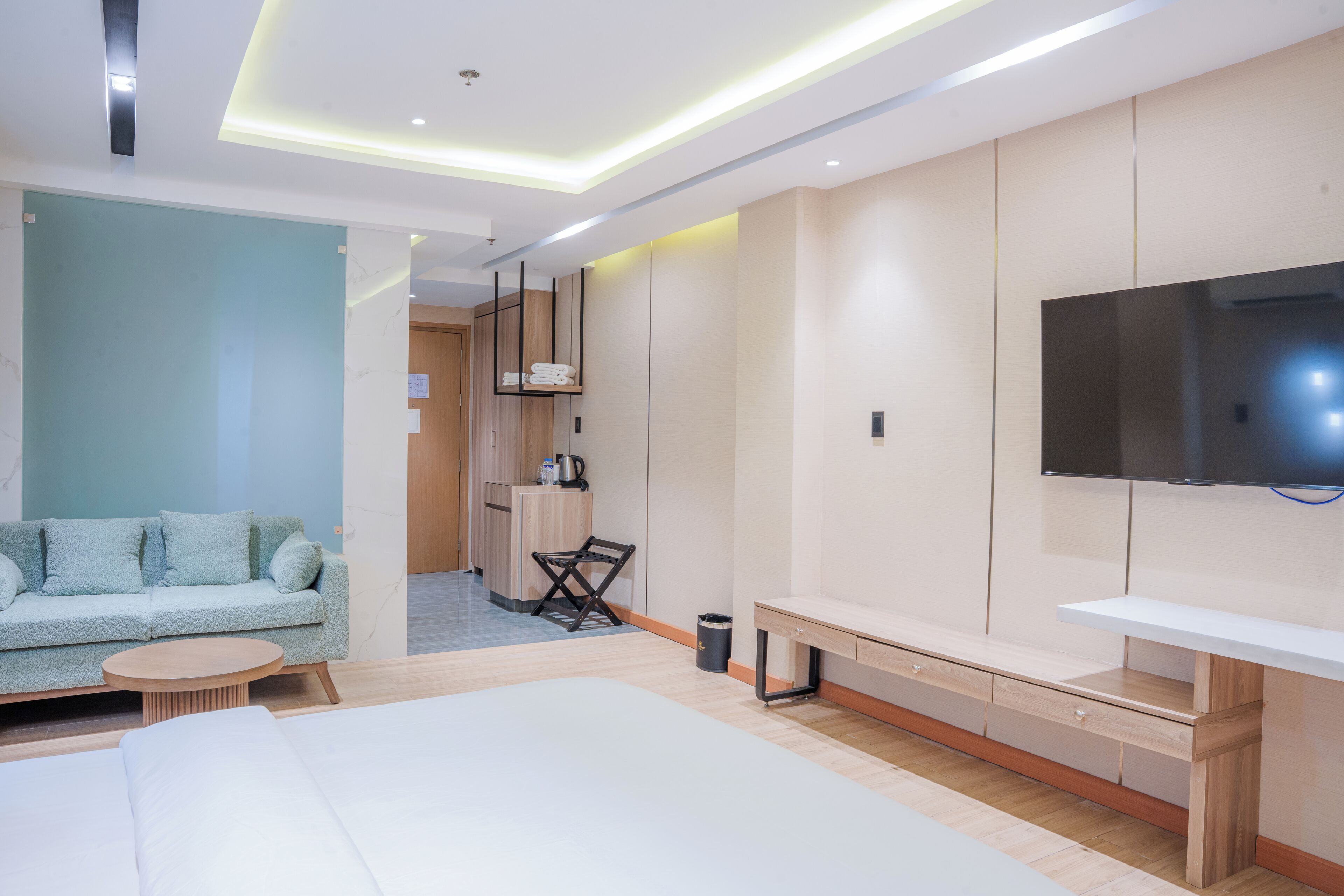 Una habitación de hotel moderna con cama, sofá, televisor y una pequeña cocina.