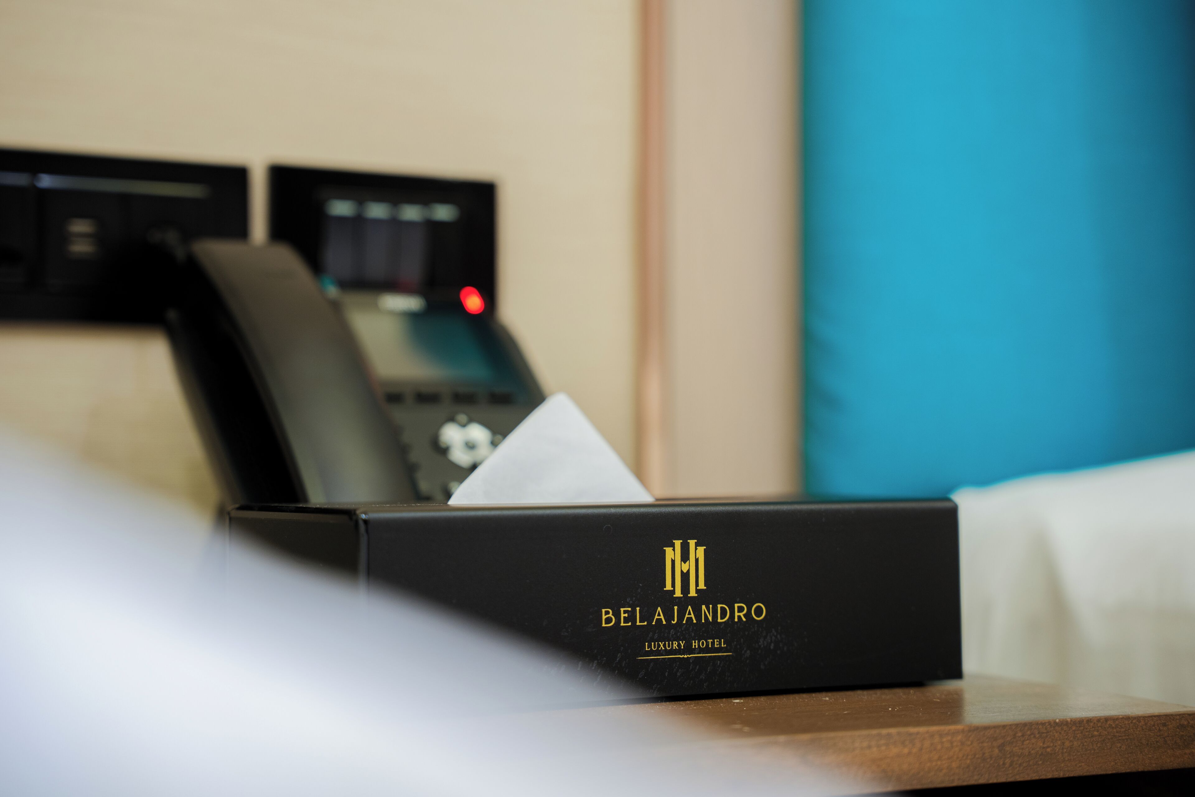 Una caja negra con el texto 'BELAJANDRO LUXURY HOTEL', un teléfono negro y un pañuelo blanco sobre una superficie de madera.