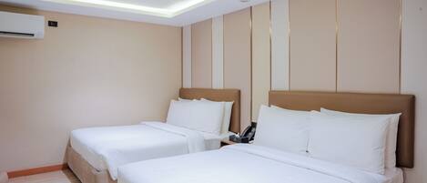 Een hotelkamer met twee bedden, een nachtkastje met een telefoon, en een airconditioning aan de muur.