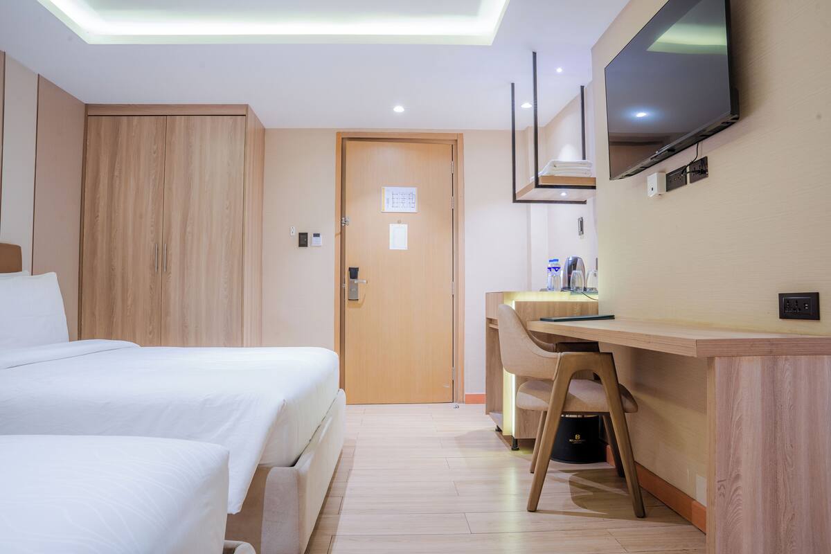 A hotel room with two beds, a desk, a chair, a television, and a door.