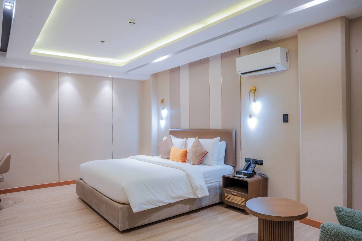 A modern hotel room with a large bed, bedside tables, an air conditioning unit, and a small round table.