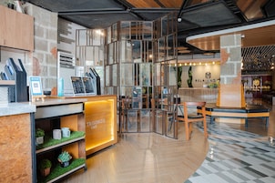 A modern hotel lobby with a reception desk, seating area, and a staircase.