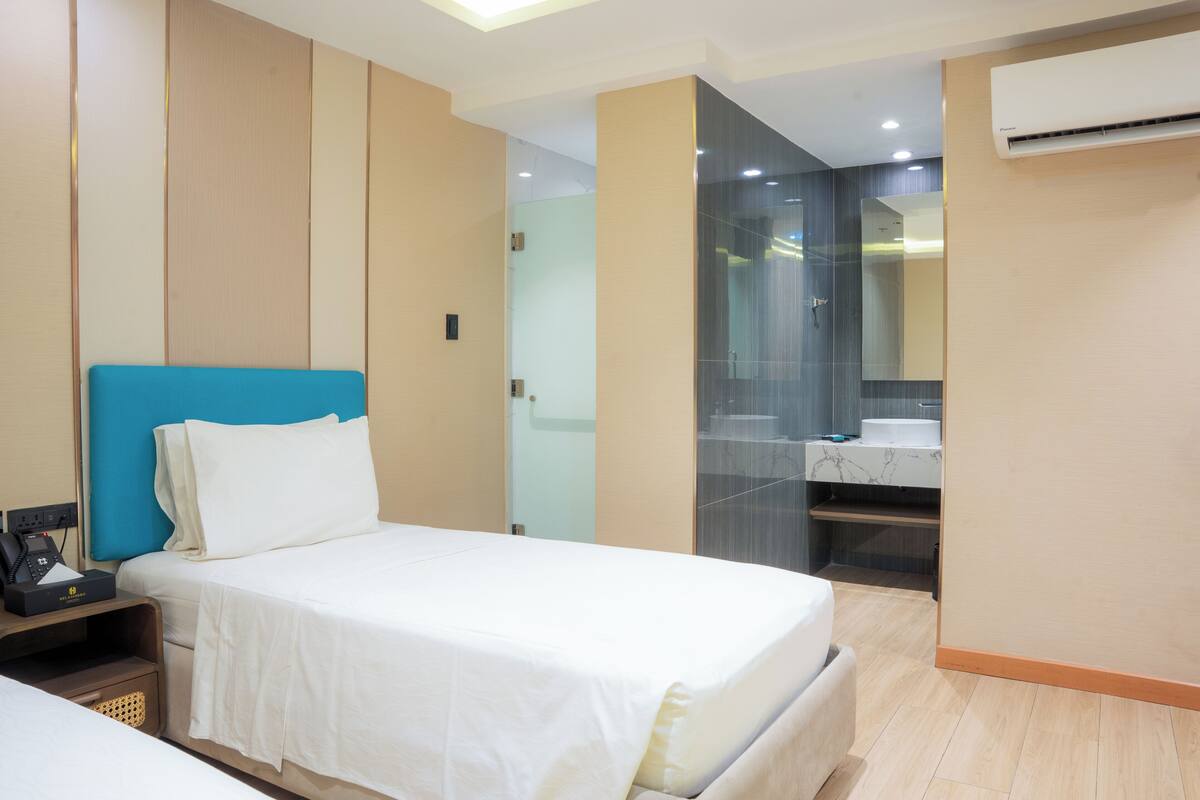 A hotel room with a bed, a bedside table with a phone, a mirror, and a bathroom with a sink and glass shower.