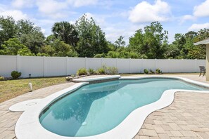 Une piscine à bord incurvé, entourée d’une terrasse en briques.