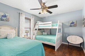 Une chambre avec des lits superposés, un ventilateur de plafond et des œuvres d’art accrochées aux murs.
