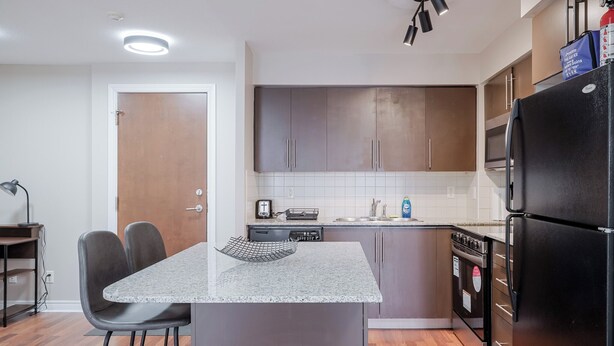 Una cocina moderna con una isla central, armarios oscuros y electrodomésticos de acero inoxidable.