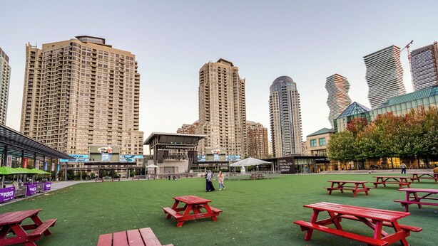 A park with red picnic tables and a stage in the center, surrounded by tall buildings. - Luxurious 2Bedroom 1Bath Condo Walk to Square One Mall YYZToronto Pearson 1 pkng (Mississauga)