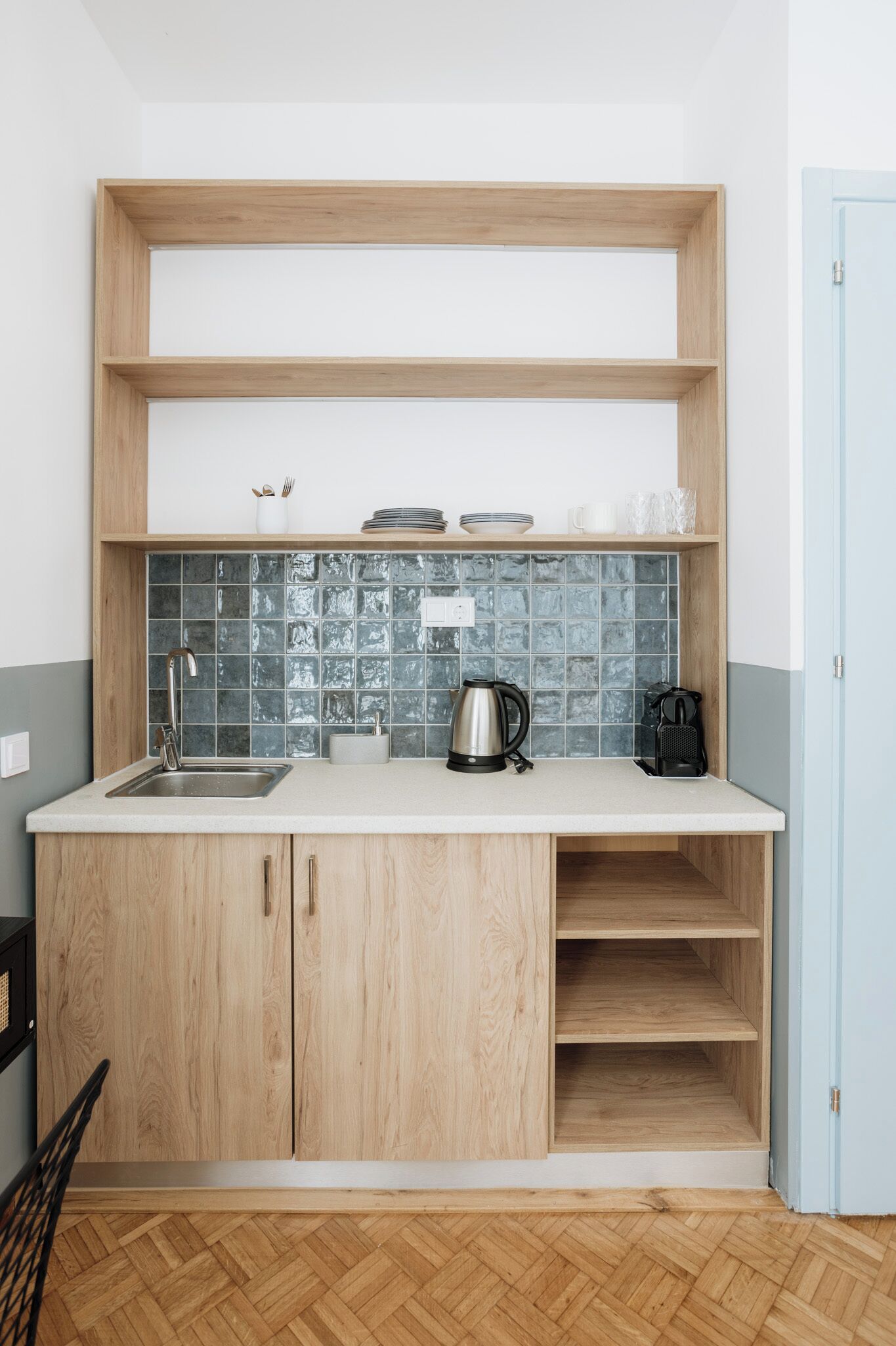 Een kleine keuken met houten kastjes, een betegelde achterwand en een aanrecht met waterkoker en koffiezetapparaat.