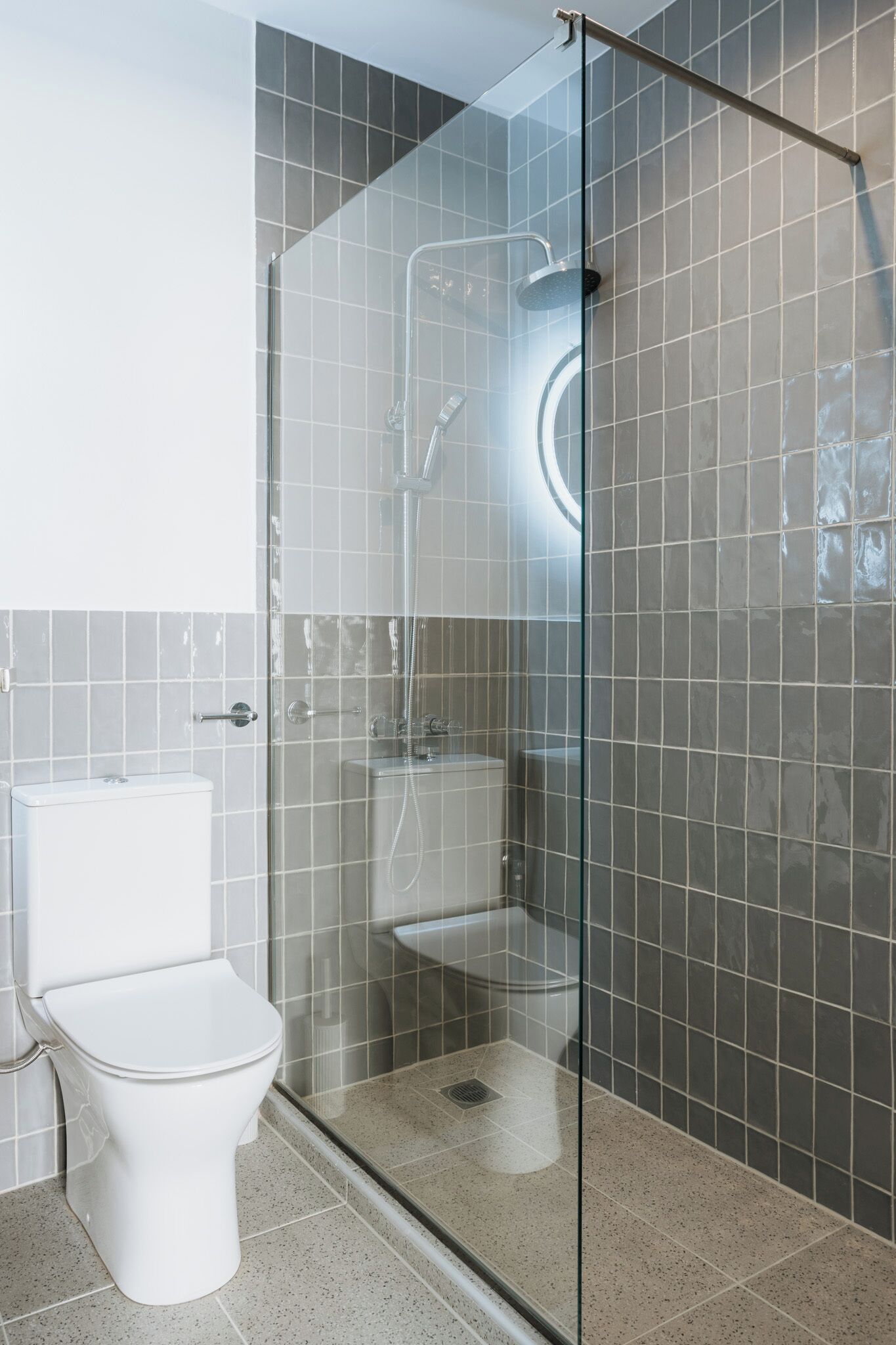 Une salle de bain moderne avec une douche à parois de verre, des toilettes blanches et des murs carrelés.