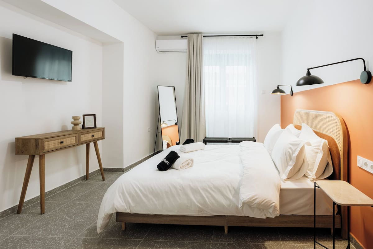 Hotellihuone, jossa on sänky, yöpöytä, televisio ja ikkuna, jossa on verhot.