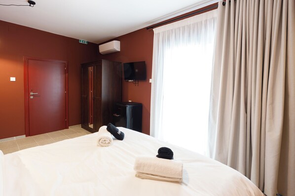 A hotel room with a bed, a TV, a wardrobe, and a door. - Canvas Color Your Stay (Volos)