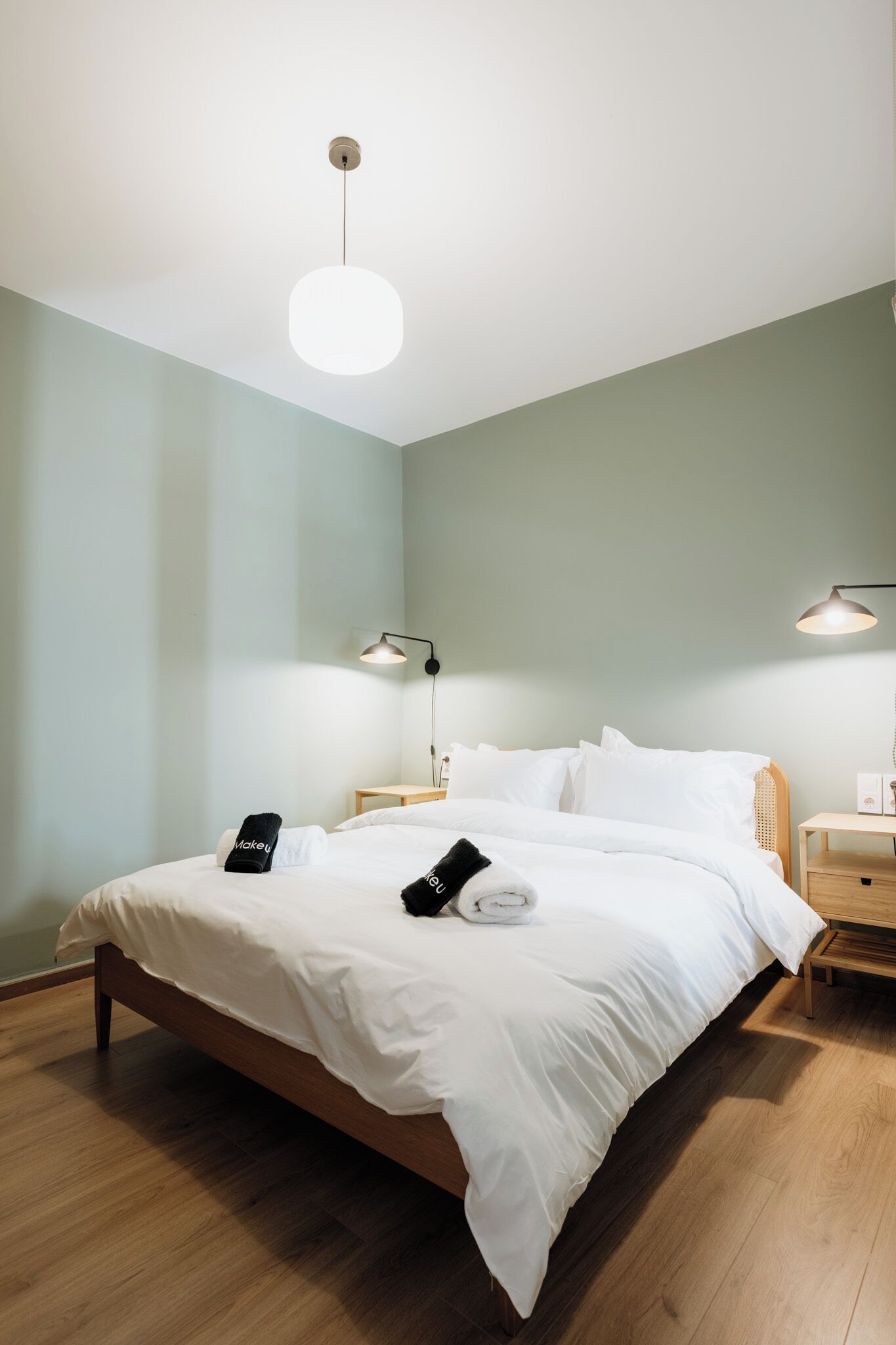 A neatly made bed with white linens, a bedside lamp, and a wooden nightstand.