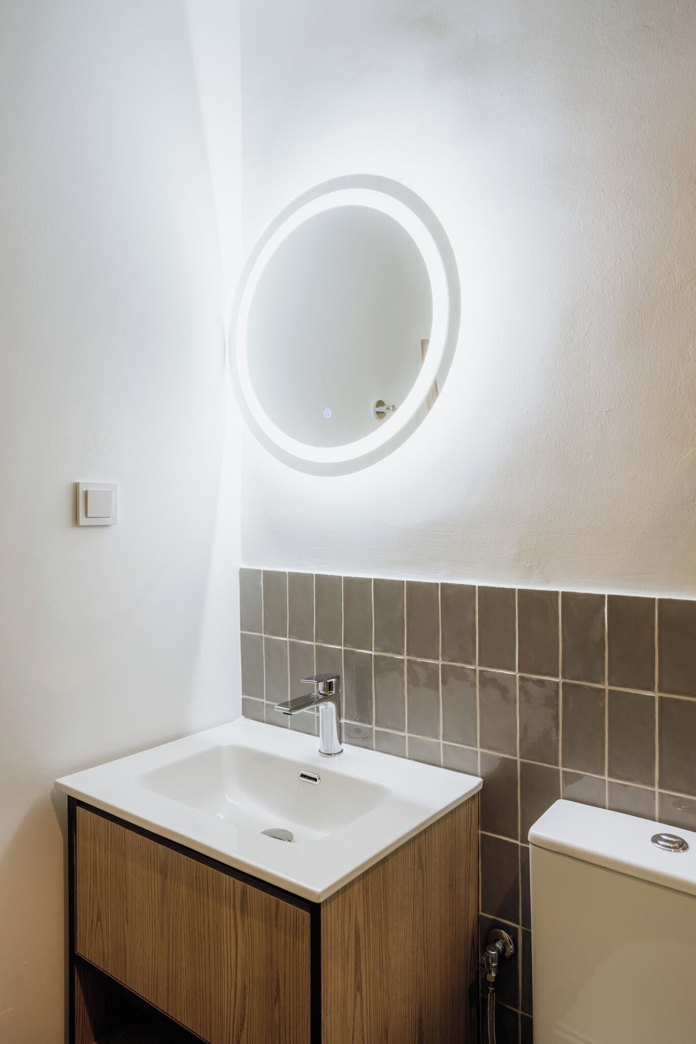 A bathroom with a white sink, a mirror with a circular light, and a toilet.