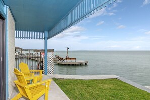 A covered outdoor area with yellow chairs, a dock extending into calm water, and a clear view of the sea.