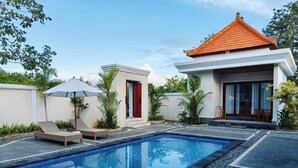 A swimming pool with lounge chairs, a small building with a red roof, and surrounding greenery. - Puri Agastya Ungasan (Ungasan)