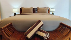 Een net opgemaakt bed met een grote, neutraal gekleurde deken en twee kussens. Aan beide zijden van het bed staan twee houten nachtkastjes met lampen.