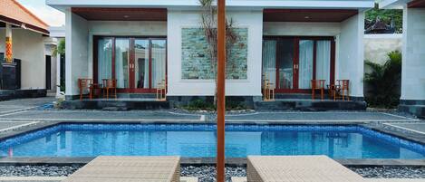 Una piscina al aire libre, sombrillas, sillones reclinables de piscina