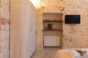 A room with a white wardrobe, a shelf with books and decorative items, a flat-screen TV, and a radiator. - Masseria Pezza La Spina (Ostuni)