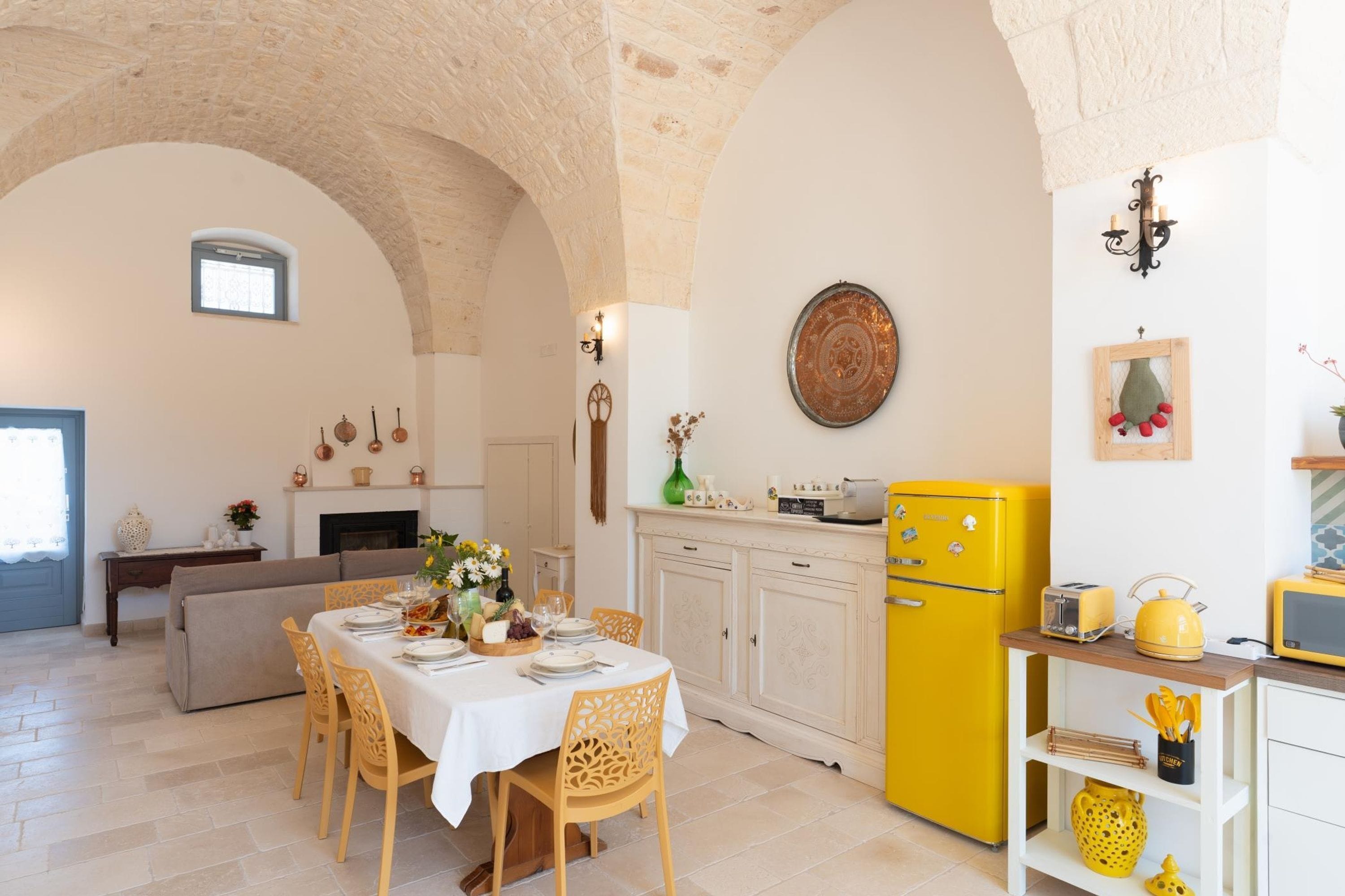 A dining area with a table set for four, a yellow refrigerator, and a kitchen area with a microwave.