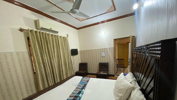 A hotel room with a large bed, a ceiling fan, an air conditioning unit, two chairs, and a small table. - Luxury Guest House (Islamabad)