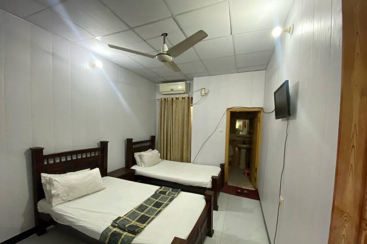 Een kamer met twee houten bedden, een plafondventilator, een airconditioner en een kleine spiegel in de hoek.