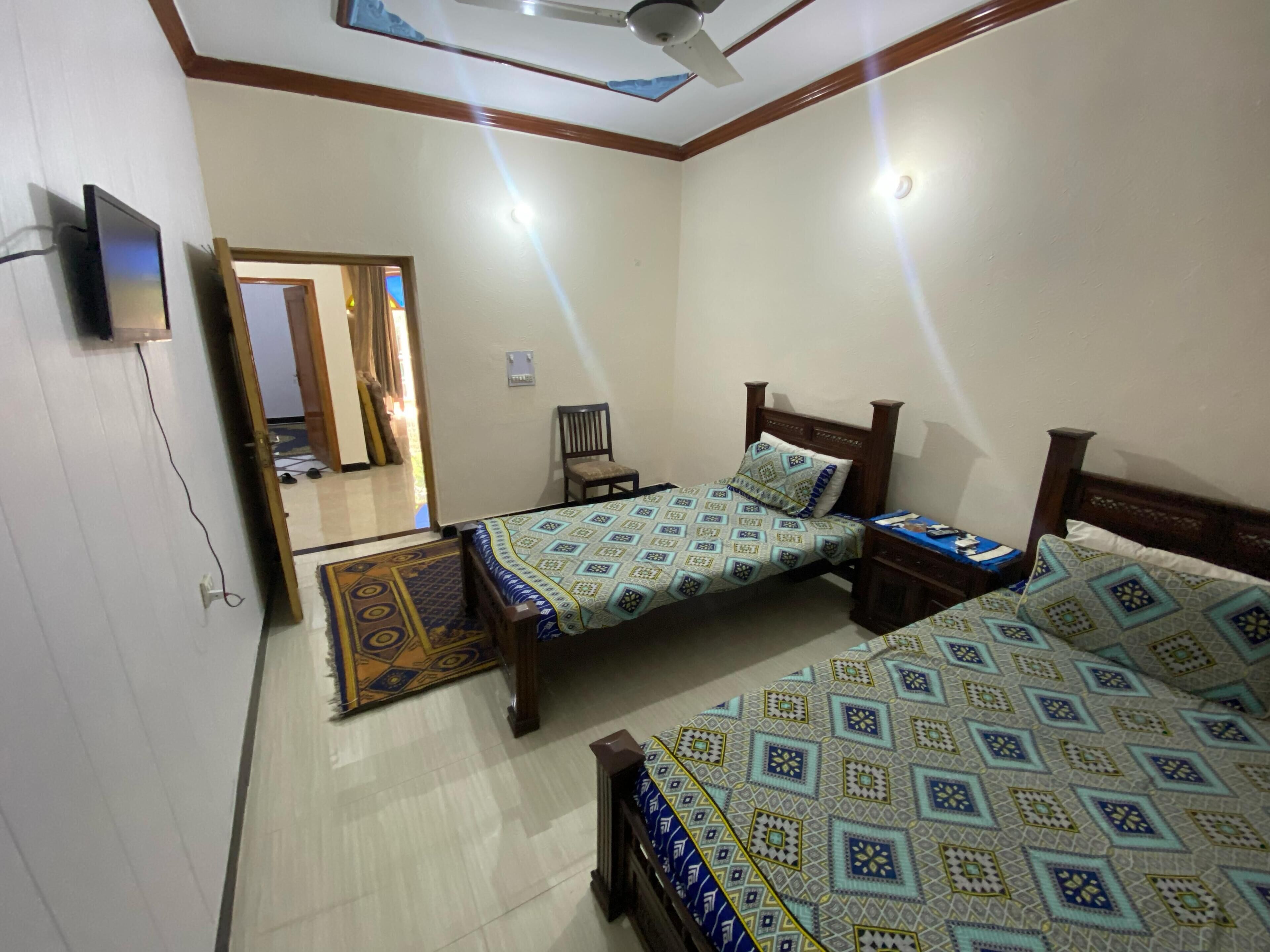 A bedroom with two beds, a ceiling fan, a TV, and a patterned rug.