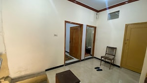 A room with a wooden door, a chair, a small table, and a pair of slippers on the floor. - Luxury Guest House (Islamabad)