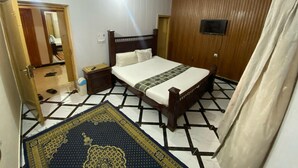 A bedroom with a bed, a nightstand, a wooden wardrobe, a ceiling fan, and a patterned rug. - Luxury Guest House (Islamabad)