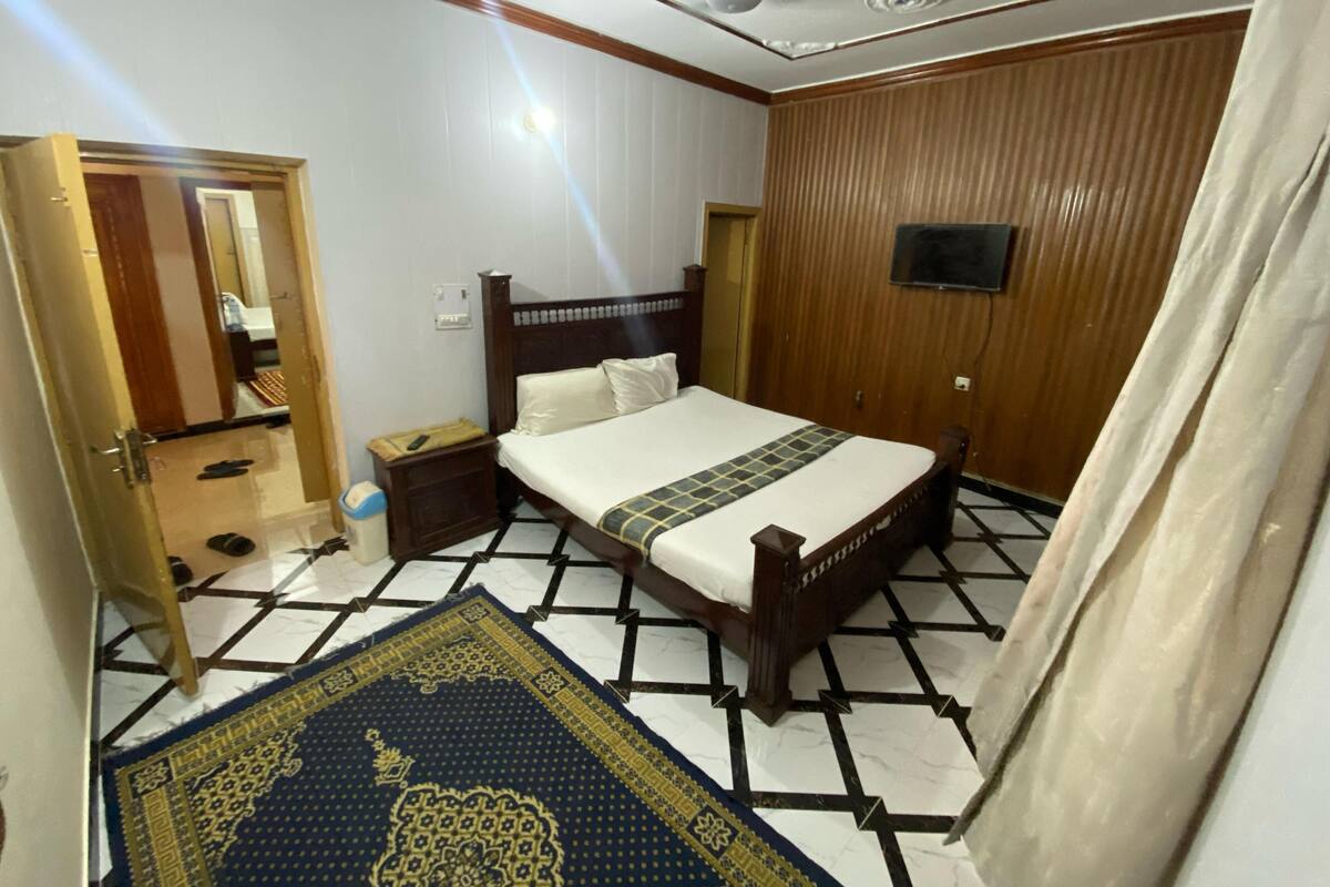 Een slaapkamer met een bed, nachtkastje, houten garderobe, plafondventilator en een kamerbreed tapijt met dessin.