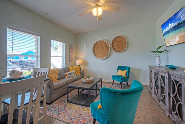 A living room with a sofa, teal armchairs, a coffee table, and a dining area with chairs and a table. - Sleeps 10 | Two Condos. Pet-Friendly + Beach access (Port Aransas)